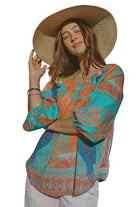 Woman wearing a colorful patterned shirt and straw hat standing in front of a statue.
